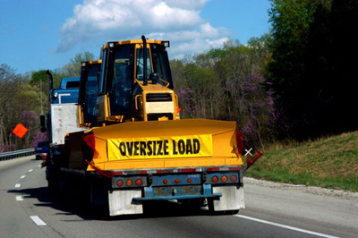 18-wheeler driving a bulldozer with an oversize load sign
