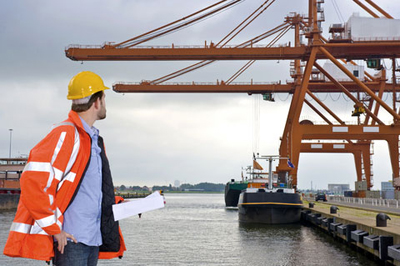 a man in protective gear inspects the loading of cargo onto a cargo ship at the dock as an example of drayage